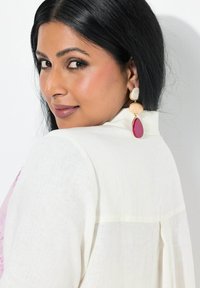 Chemise en lin blanc avec un empiècement et des détails plissés, associée à des boucles d'oreilles colorées — crème, pêche et fuchsia en formes de goutte et ovales.