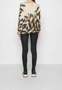 Pullover in hellem Creme mit einem dunkelbraunen und senfgelben Blattmuster; kombiniert mit dunkelblauen Skinny-Jeans und schwarzen Plateau-Stiefeln.