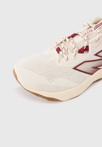 Chaussure de course légère en crème avec des accents bordeaux, tige en mesh pour la respirabilité, semelle extérieure texturée pour l'adhérence et renfort à l'avant du pied.