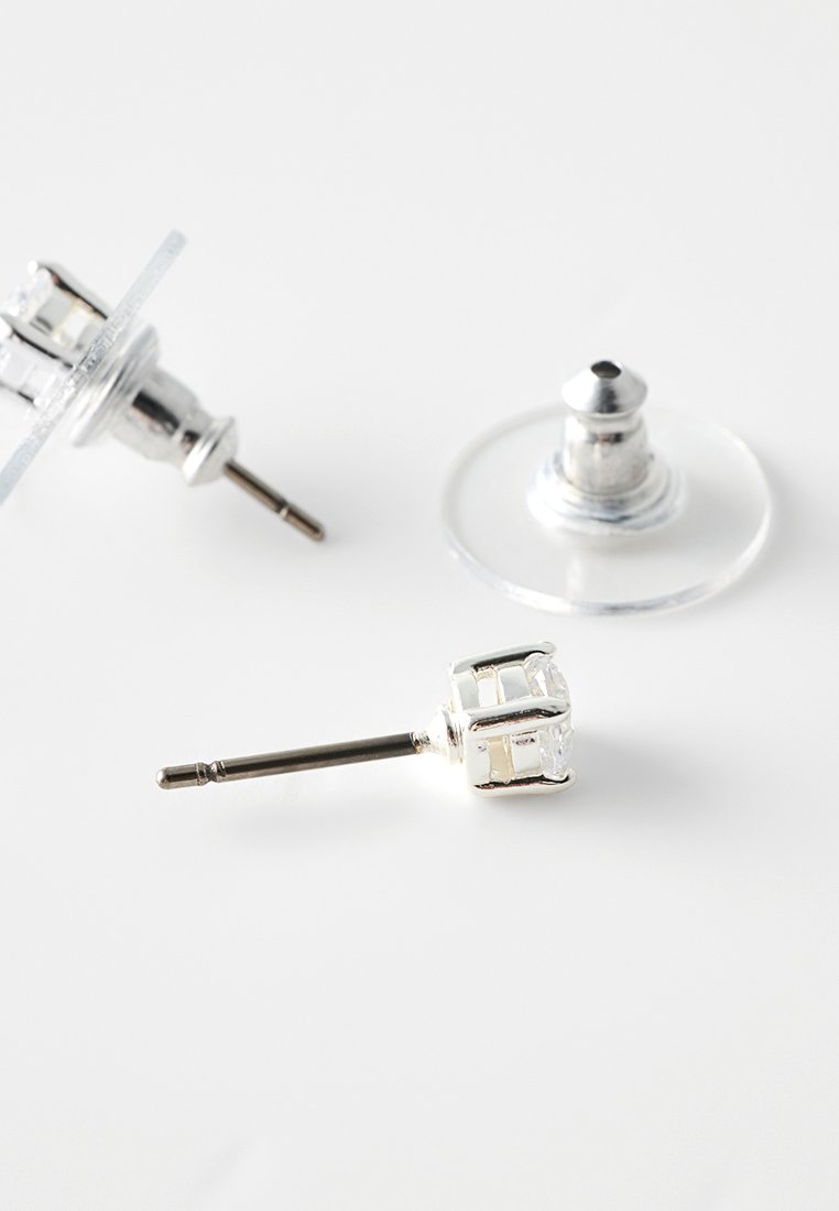 Silberner Ohrstecker mit klarem Edelstein und transparentem Schmetterlingsverschluss auf einer weißen Oberfläche.