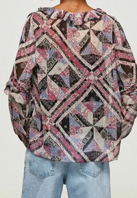 Genomskinlig blus i ett lapptäckesdesign med rosa, svart och blå mönster. Rynkad halslinning och lös passform med långa puffärmar.