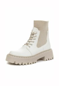 Chunky white ankle boot with a beige ribbed knit upper, rounded toe, lace-up front, and thick textured rubber sole with grooves.