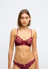Bralette en dentelle bordeaux avec des bretelles réglables, présentant des motifs floraux et des bords en dentelle festonnée, accompagné d'un string en dentelle assorti.