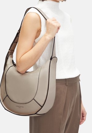 Pehmeä nahkainen olkalaukku vaaleanharmaana, mustin yksityiskohdin. Laukussa on kaareva muoto ja säädettävä hihna. Edessä näkyy brändäys.
