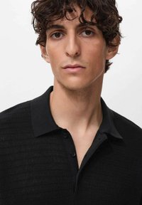 Polo nero con un design a maglia tessurizzata, dotato di colletto e chiusura con tre bottoni. Il tessuto appare morbido e leggermente elasticizzato.