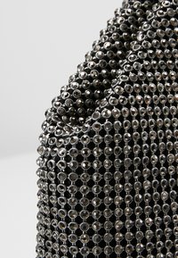 Tissu noir densément couvert de clous métalliques ronds et brillants disposés en motif quadrillé avec des surfaces réfléchissantes.