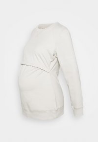Sudadera de maternidad en color crema, confeccionada en tejido suave. Presenta mangas largas, un escote redondeado y una banda fruncida en la cintura para mayor elasticidad.