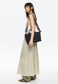 Czarna prostokątna torba z dwoma uchwytami i regulowanym paskiem. Gładka tekstura, minimalistyczny design i subtelne oznakowanie z przodu.