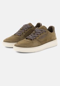 Paire de baskets basses en daim olive avec des lacets gris et des semelles en caoutchouc blanc, inclinées légèrement vers la gauche sur un fond blanc.