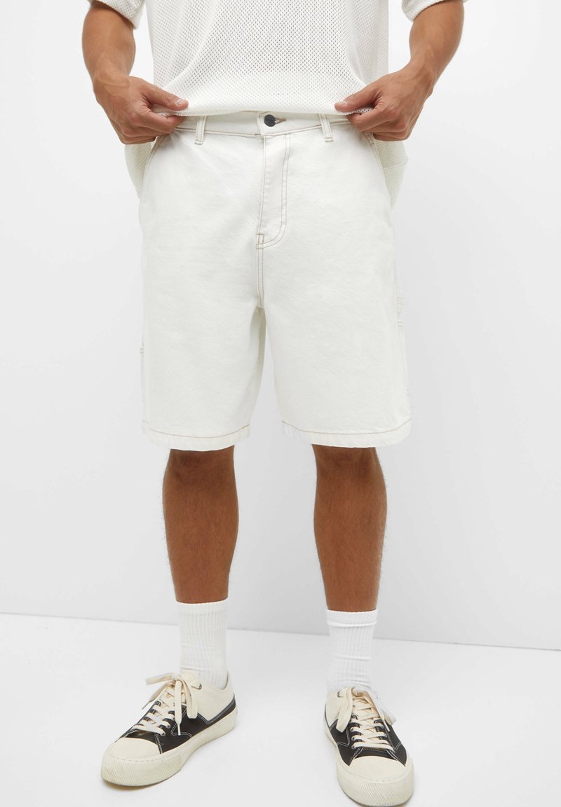 Shorts cargo de mezclilla blanca con corte recto, que presentan bolsillos laterales y costuras visibles. Combinados con zapatillas en blanco y negro.