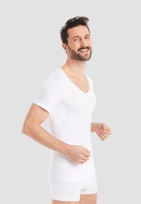 White short-sleeve undershirt with a V-neck design and textured fabric, featuring discreet underarm panels for additional coverage.