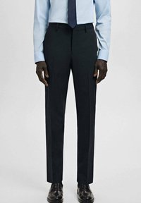 Granatowe spodnie w kant o gładkiej fakturze, z płaskim przodem i prasowanymi kantami. W połączeniu z jasnoniebieską koszulą i czarnymi wypastowanymi butami.