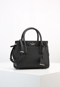 Borsa Kate Spade in pelle nera texturizzata con manici doppi, tracolla regolabile e etichetta pendente su superficie bianca.