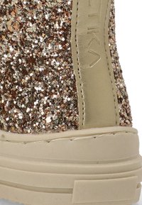 Partes superiores de zapato en oro rosa brillante con un acabado texturizado, suela de goma beige y un acento de cuero en contraste en el lado.