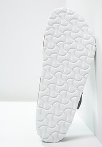 Semelle de sneaker blanche avec un motif de vagues texturé, présentant un dessus gris clair et des touches de marron. Profil latéral sur fond uni.