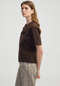Bruine korte mouwen t-shirt met een ronde hals en gestructureerde letters op de voorkant. Gepaard met lichtgekleurde, patroonbroeken.