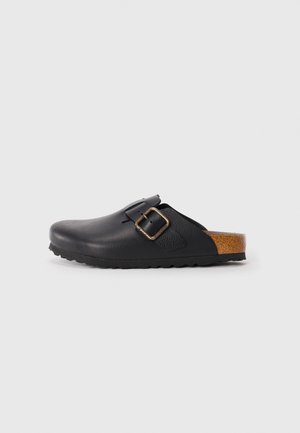 Black leather clogs with a textured surface, featuring a single adjustable strap with a gold buckle and a cork accent on the heel.