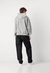 Sudadera gris con capucha, de corte relajado, con mangas con puños, combinada con pantalones vaqueros oscuros de corte holgado y zapatillas blancas.
