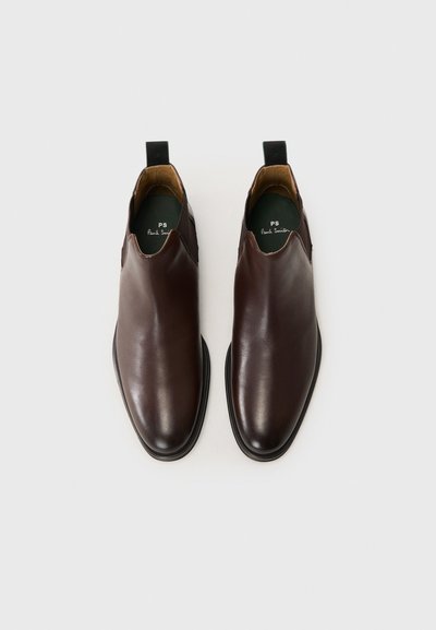 Chaussures en cuir marron à enfiler avec une finition lisse, forme de pied en amande, petit talon et un tirant arrière noir contrastant. L'intérieur présente un revêtement vert.