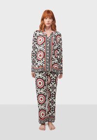 Conjunto de pijama estampado con un diseño en negro, blanco y rojo, con motivos circulares. Está hecho de una tela ligera, tiene un corte relajado y mangas largas.
