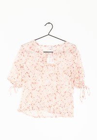 Blusa a maniche corte rosa con fantasia floreale, scollatura a chiave, legature arricciate sulle maniche e tessuto leggero e trasparente. Presenta motivi paisley e fiori.