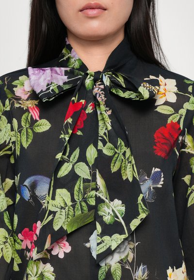 Floral blouse in black fabric featuring vibrant red, purple, and white flowers, with a bow tie collar and green leaves detailed throughout.