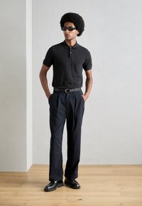 Svart polo-skjorte med korte ermer, kombinert med navy stripete bukser. Svart belte og sko. Glatte teksturer og en tettsittende silhuett.