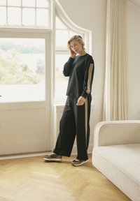 Luźny czarny sweatshirt z beżowym akcentem na rękawie, w połączeniu z czarnymi spodniami o szerokich nogawkach. Brązowe i beżowe sneakersy dopełniają całość.