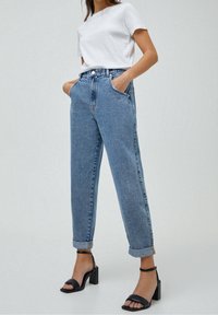 Jeans de tiro alto en azul claro, con piernas rectas, puños doblados y bolsillos laterales, combinados con una camiseta blanca lisa de manga corta y tacones negros.