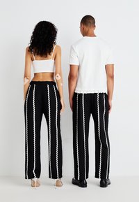 Pantalones de pierna ancha negros con rayas zigzagueantes blancas. Combinado con un top corto blanco. Modelo de espaldas frente a la cámara, mostrando un ajuste relajado.
