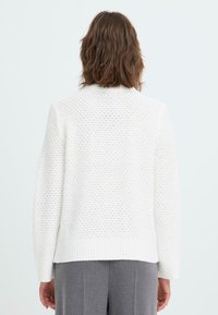 White knitted sweater with a textured pattern, featuring a ribbed hem and cuffs. The design has a classic crew neck and long sleeves.