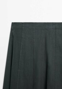Jupe vert foncé avec des détails de coutures verticales et une taille haute sur un fond blanc uni.