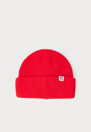 Red knitted beanie with a ribbed texture, featuring a folded cuff and a small white tag with a logo. Smooth, close-fitting design.
