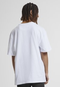 T-shirt en coton blanc oversize avec des manches courtes, un col rond et une texture lisse, vue de l'arrière. Aucun motif ni graphique visible.