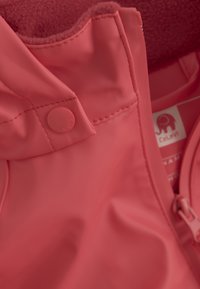 Rode waterdichte jas met een soepele textuur, een ronde knoopsluiting en een zachte binnenvoering. Voorzien van een merklabel met een olifantenlogo.