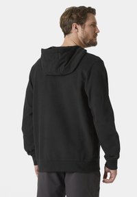 El hoodie de algodón negro cuenta con una capucha amplia, puños y dobladillo acanalados, con un ajuste relajado y una textura suave. La vista trasera revela detalles mínimos.