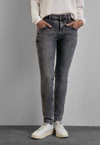 Jean en denim gris à coupe slim, taille haute, poches avant et détails de décoloration subtils, associés à des baskets blanches.