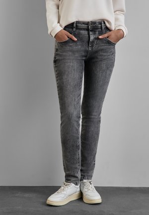 Jeans de mezclilla gris con corte ajustado, cintura alta, bolsillos frontales y detalles de decoloración sutil, combinados con zapatillas blancas.