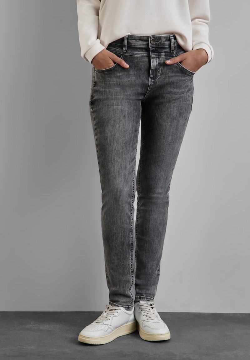 Jean en denim gris à coupe slim, taille haute, poches avant et détails de décoloration subtils, associés à des baskets blanches.