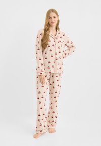 El conjunto de pijama de algodón presenta rayas rosas y blancas con estampados de cerezas; incluye mangas largas, un bolsillo en el pecho y pantalones de corte holgado.