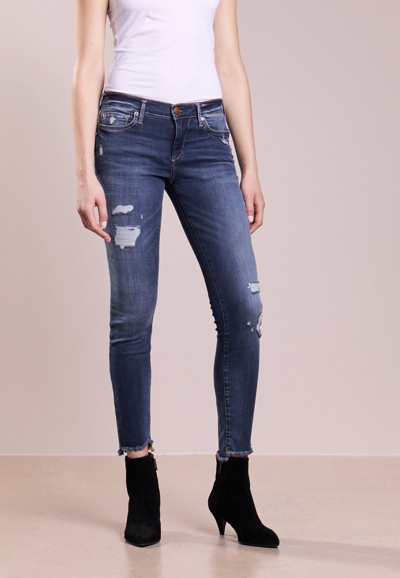 Tmavě modré skinny džíny s popraskanými otvory, třepenými manžetami a středním pasem. V kombinaci s černými kotníkovými botami.