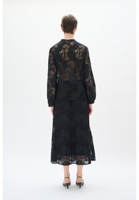 Schwarzes Spitzenkleid mit langen Ärmeln und einer Länge bis zur Mitte der Waden, das ein filigranes Blumenmuster und eine durchsichtige Textur aufweist. Die Rückansicht zeigt einen schlichten Ausschnitt.