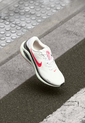 White athletic shoe with pink accents and a mesh upper, featuring a cushioned sole and visible air unit. Laced design with logo detail.