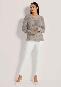 Helle graue gehäkelte Sweater mit weiten Ärmeln, kombiniert mit weißen, eng anliegenden Hosen und beigen, spitzen Absätzen. Texturiertes Design mit offener Maschenstruktur.