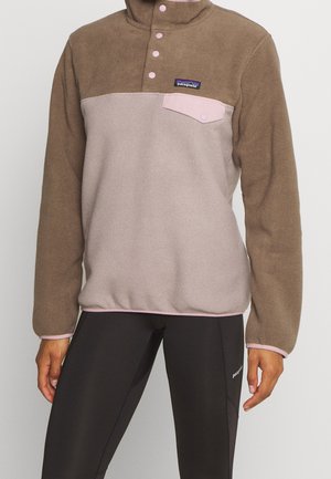 Polaire Patagonia marron et beige avec pressions roses et poche poitrine, portée avec des leggings Patagonia noirs.