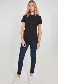 Sort polo t-shirt med korte ærmer og tre knapper ved kraven, parret med mørkeblå skinny jeans og hvide sneakers.