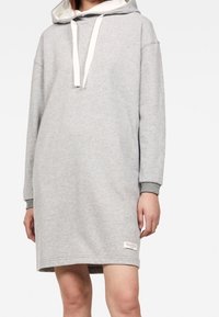 Grå huvtröja klänning med en kenguruficka, vita dragsko och ribbade ärmslut. Slät textur med en avslappnad, lös passform.