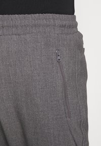 Grå joggers gjorda av texturerat material, med elastisk midja och en ficka med dragkedja på sidan. Modern och funktionell design.