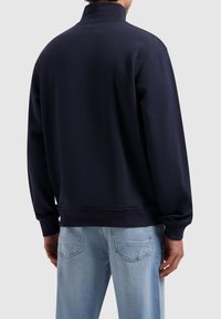 Navy blue sweatshirt with a high collar, ribbed cuffs, and hem. Smooth fabric, relaxed fit, and minimal branding detail at the back.
