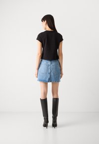Schwarzes, kurzes T-Shirt kombiniert mit einem hellen Denim-Minirock. Das Model trägt elegante schwarze Stiefel bis zum Knie. Einfaches und lässiges Design.